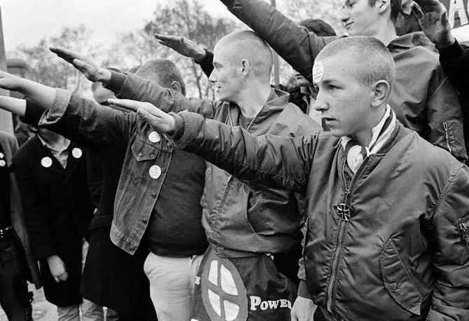 Photo en noir et blanc de jeunes skinheads faisant le salut nazi, l'un portant un badge White Power