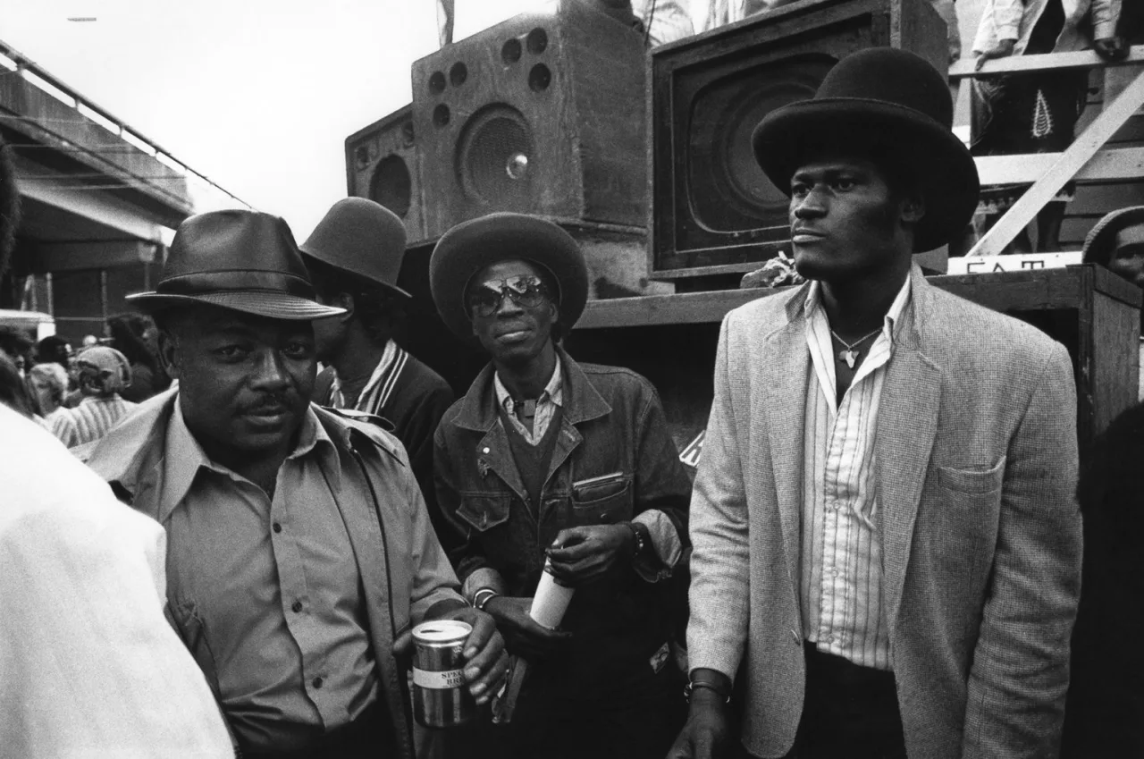 Photo en noir et blanc de plusieurs hommes noirs élégamment vêtus devant un sound system artisanal