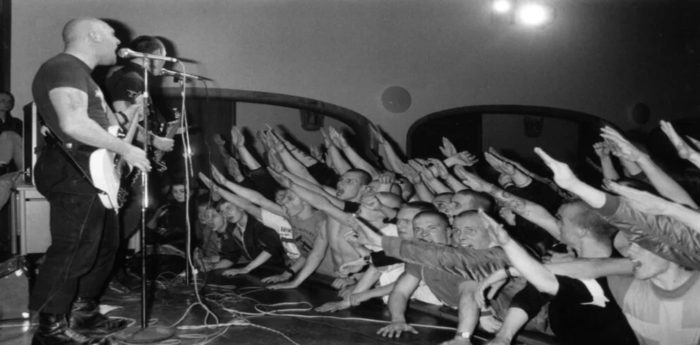 Photo en noir et blanc d'un concert de Skrewdriver, foule de skinheads faisant le salut nazi bras tendu vers la scène